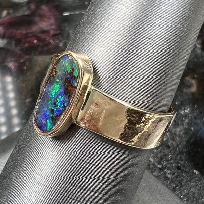 A blue green oval cabochon cut Australian boulder opal set in a yellow gold solitaire ring.