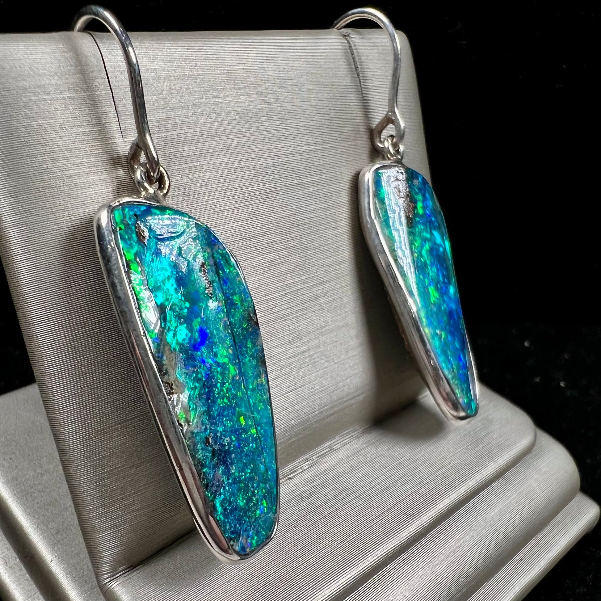 A pair of white gold boulder opal French wire dangle earrings.  The opal is predominantly glimmery blue.