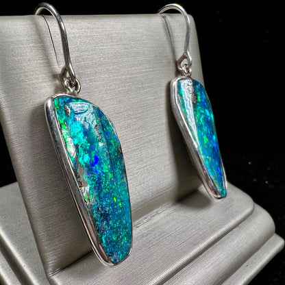 A pair of white gold boulder opal French wire dangle earrings.  The opal is predominantly glimmery blue.
