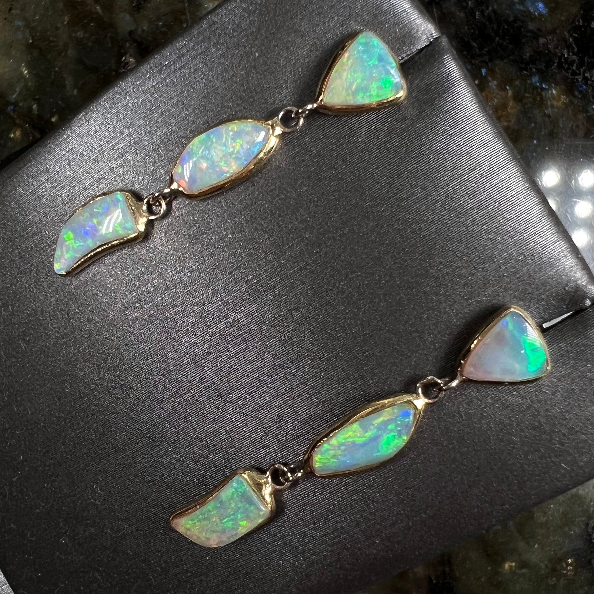 A pair of yellow gold push-back dangle earrings set with three white crystal opals in each.