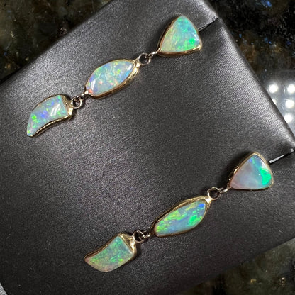 A pair of yellow gold push-back dangle earrings set with three white crystal opals in each.