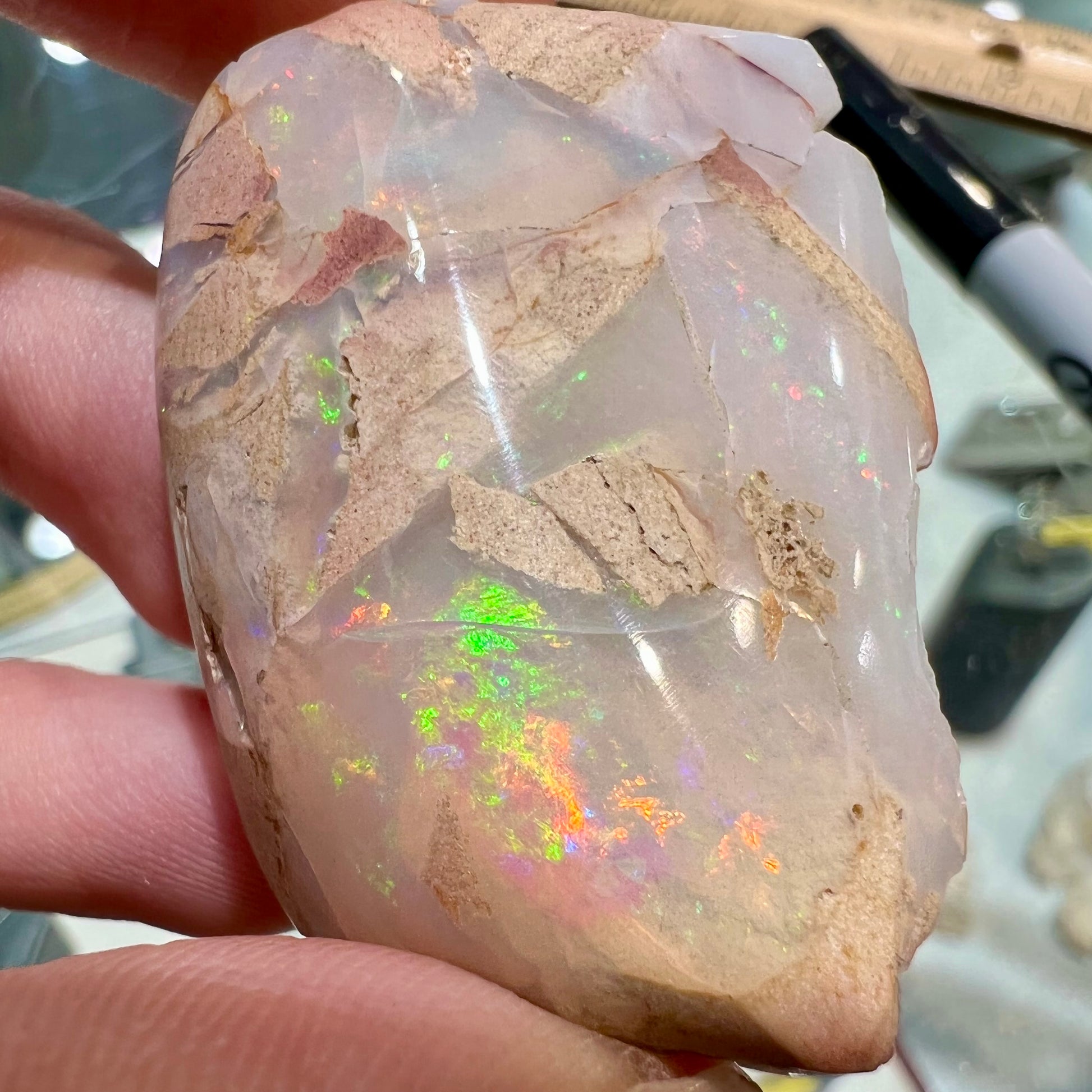 A preform polished matrix opal specimen from White Bluffs, Australia.  Predominant colors are red, green, and violet.