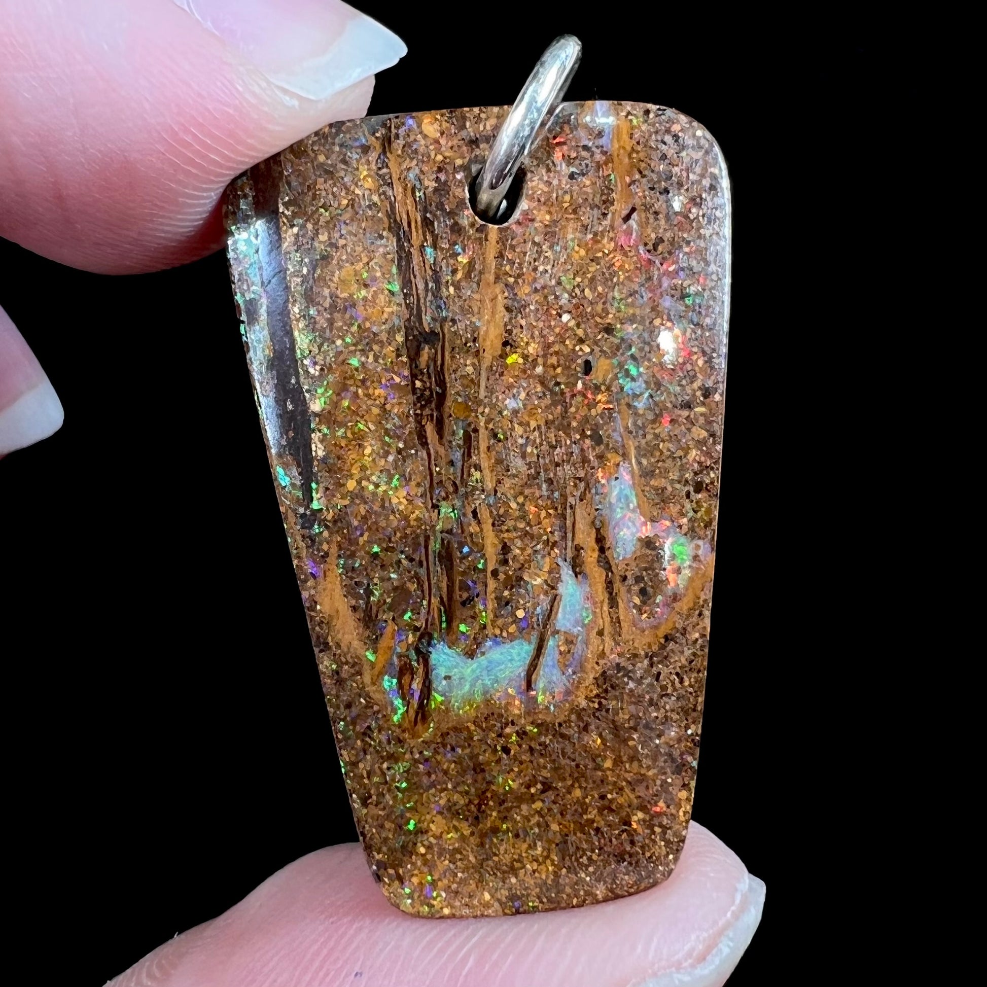 A drilled boulder opal stone with a sterling silver ring through the hole to be worn as a pendant.