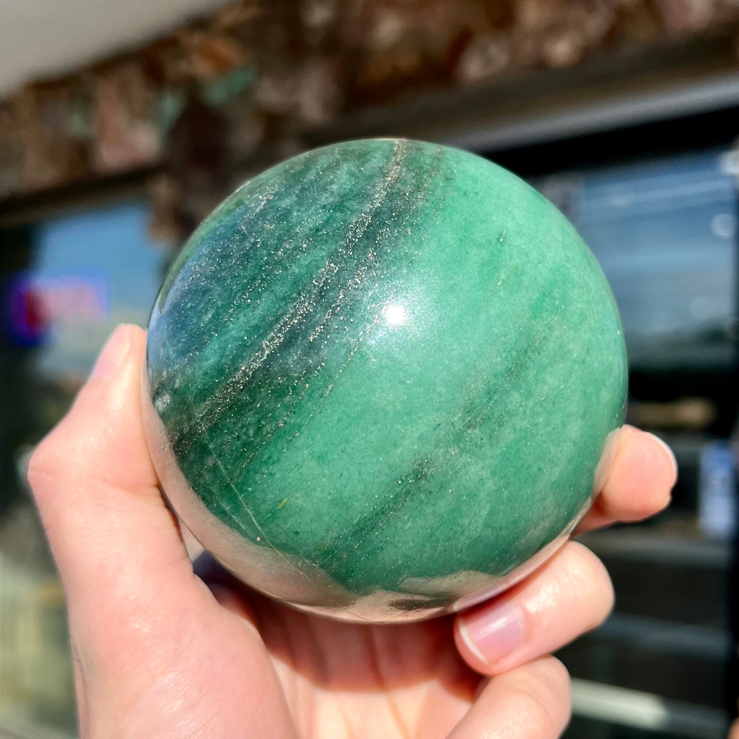 A stone sphere carved from natural green aventurine quartz with containing mica inclusions.