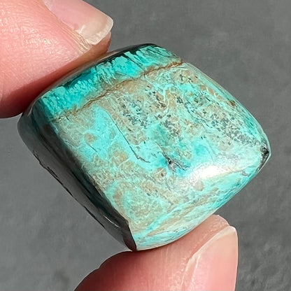 A loose, polished turquoise specimen with azurite inclusions.