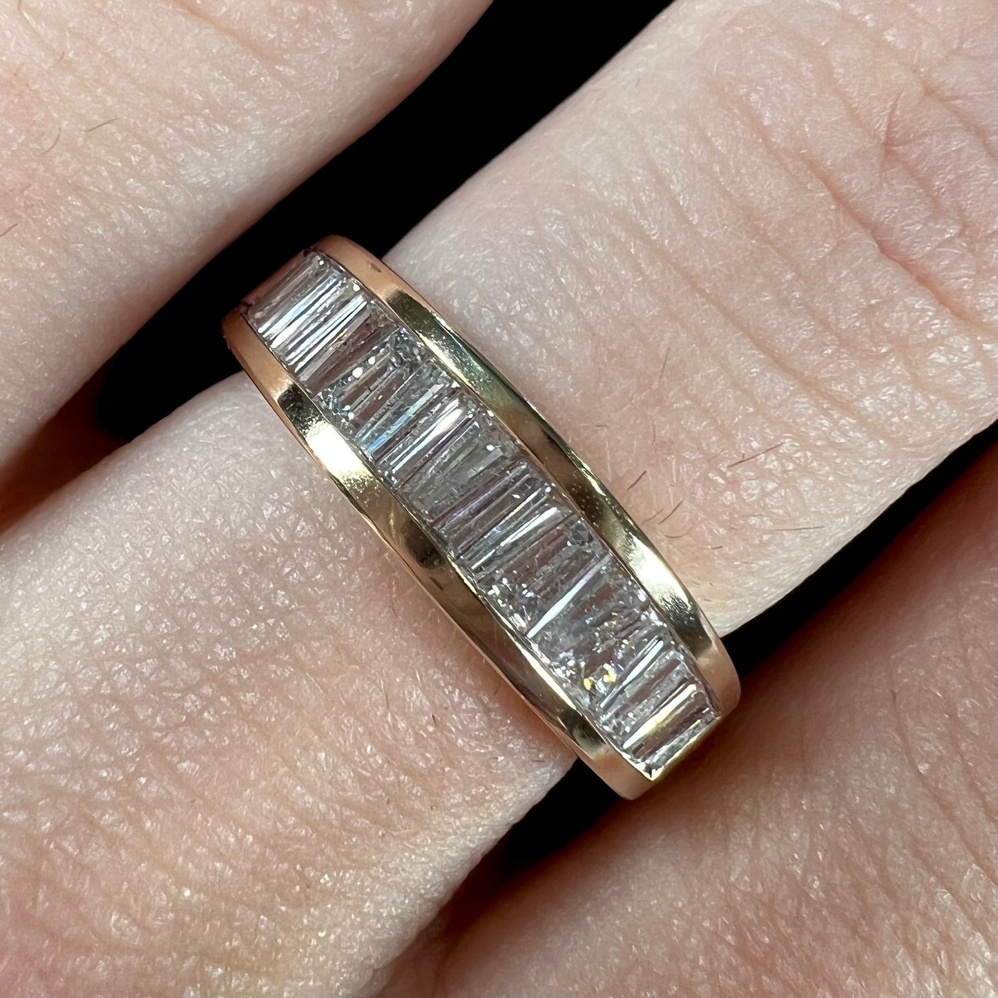 A ladies' yellow gold ring channel set with a row of baguette cut diamonds.