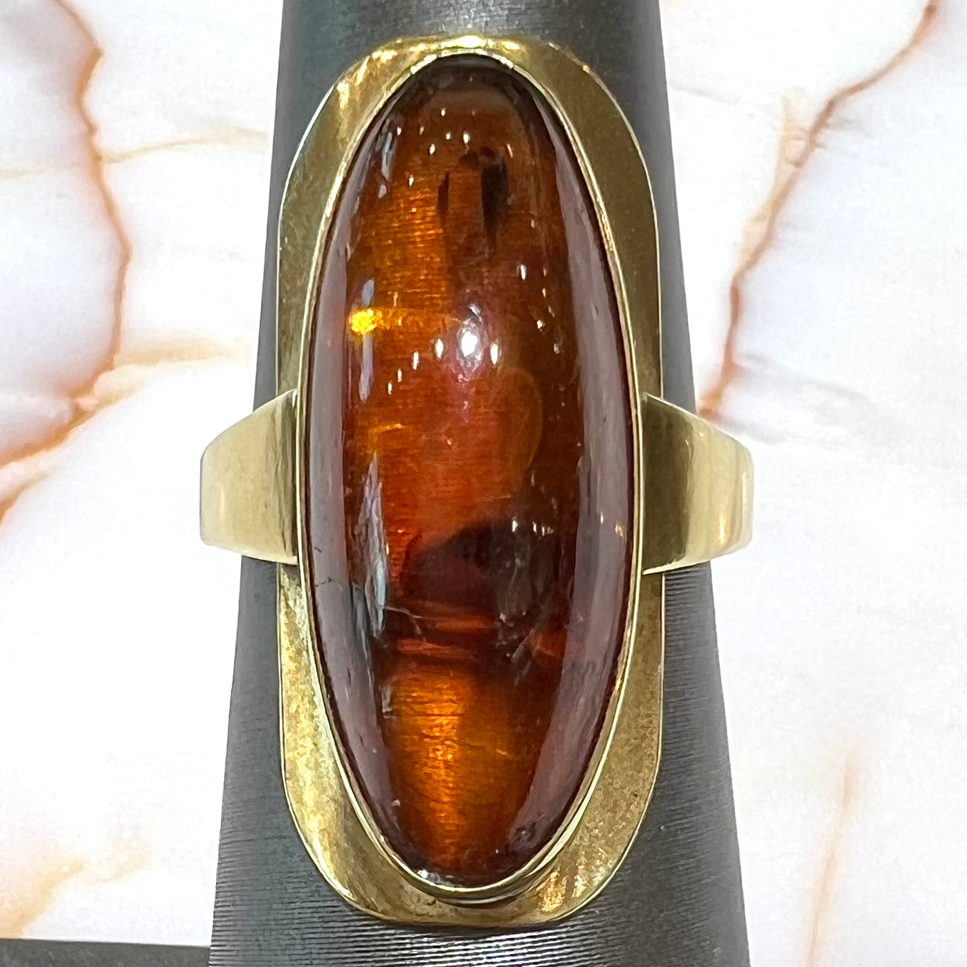 An oval cabochon cut Baltic amber stone set in a yellow gold ring and stamped "AMBER GUILD."