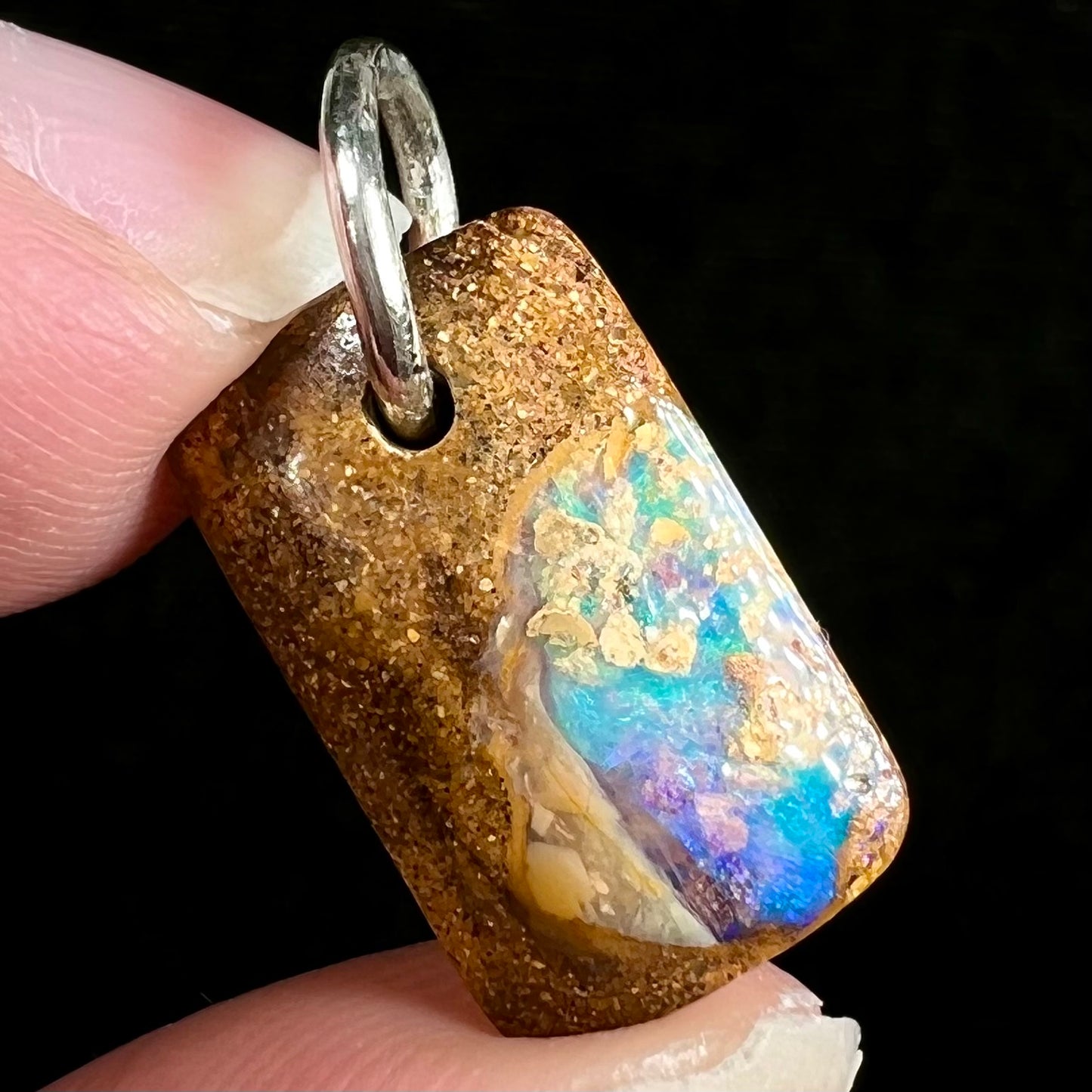 A drilled boulder opal stone with a sterling silver ring through the hole to be worn as a pendant.