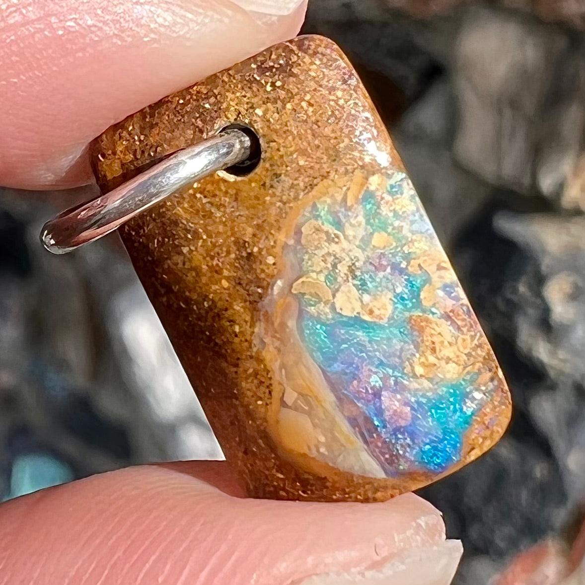 A drilled boulder opal stone with a sterling silver ring through the hole to be worn as a pendant.