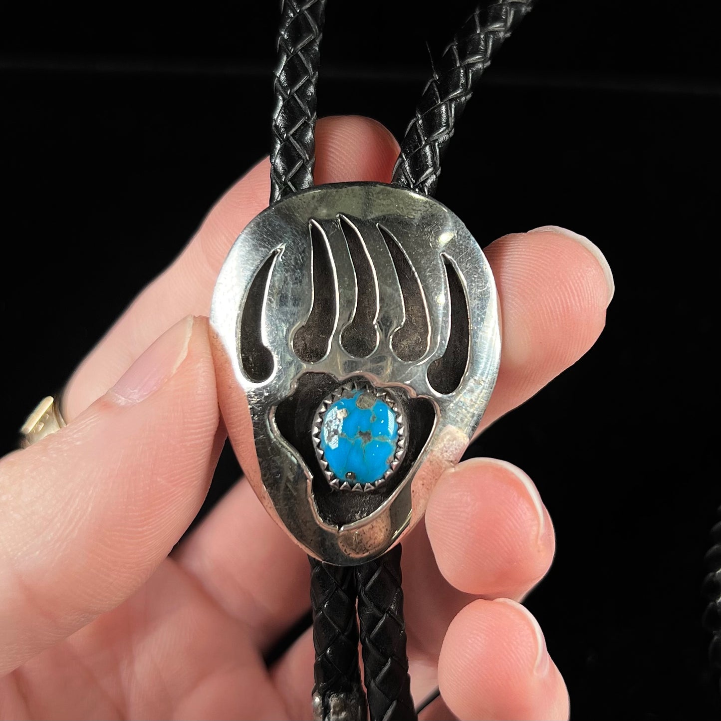 A sterling silver bolo tie in the shape of a bear's paw set with a Morenci turquoise stone.