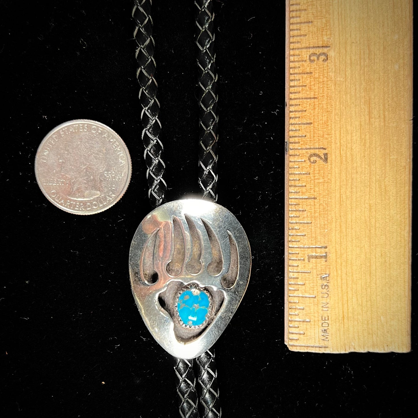 A sterling silver bolo tie in the shape of a bear's paw set with a Morenci turquoise stone.