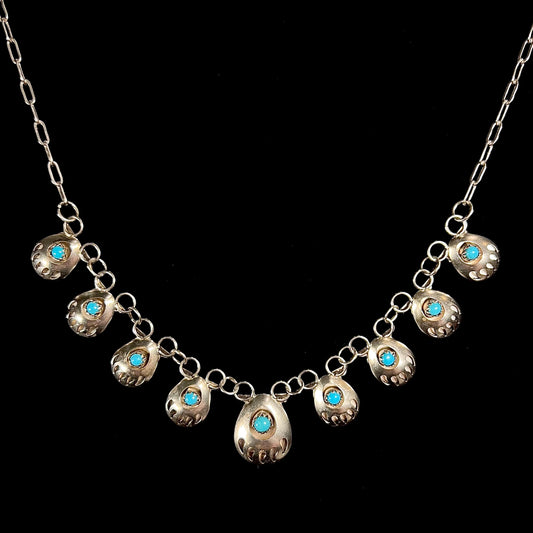 A silver turquoise necklace handmade with nine silver bear paws set with round turquoise stones.