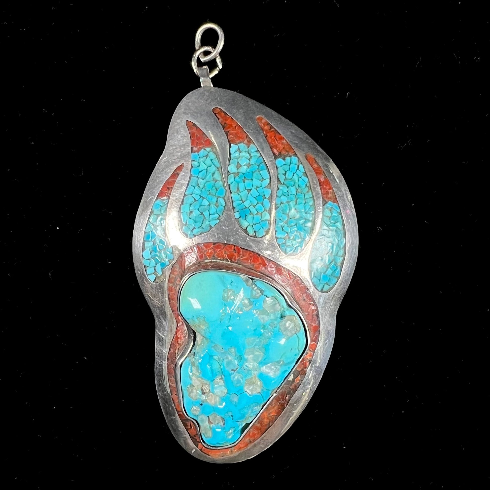 A sterling silver bear paw pendant set with Sleeping Beauty turquoise, crushed turquoise, and crushed coral.