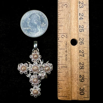 A cross pendant with floral decoration.  The cross is made of six  flowers with sterling silver petals and yellow gold nectar.  A silver bee is on one of the pendants.  The bail opens and closes.