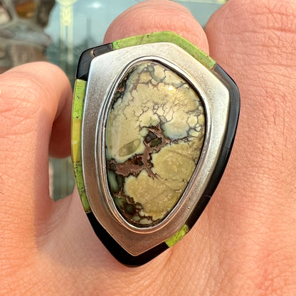 A shield shaped silver ring bezel set with a green gaspeite stone with stone inlaid edges, handmade by artist Benny Armijo.