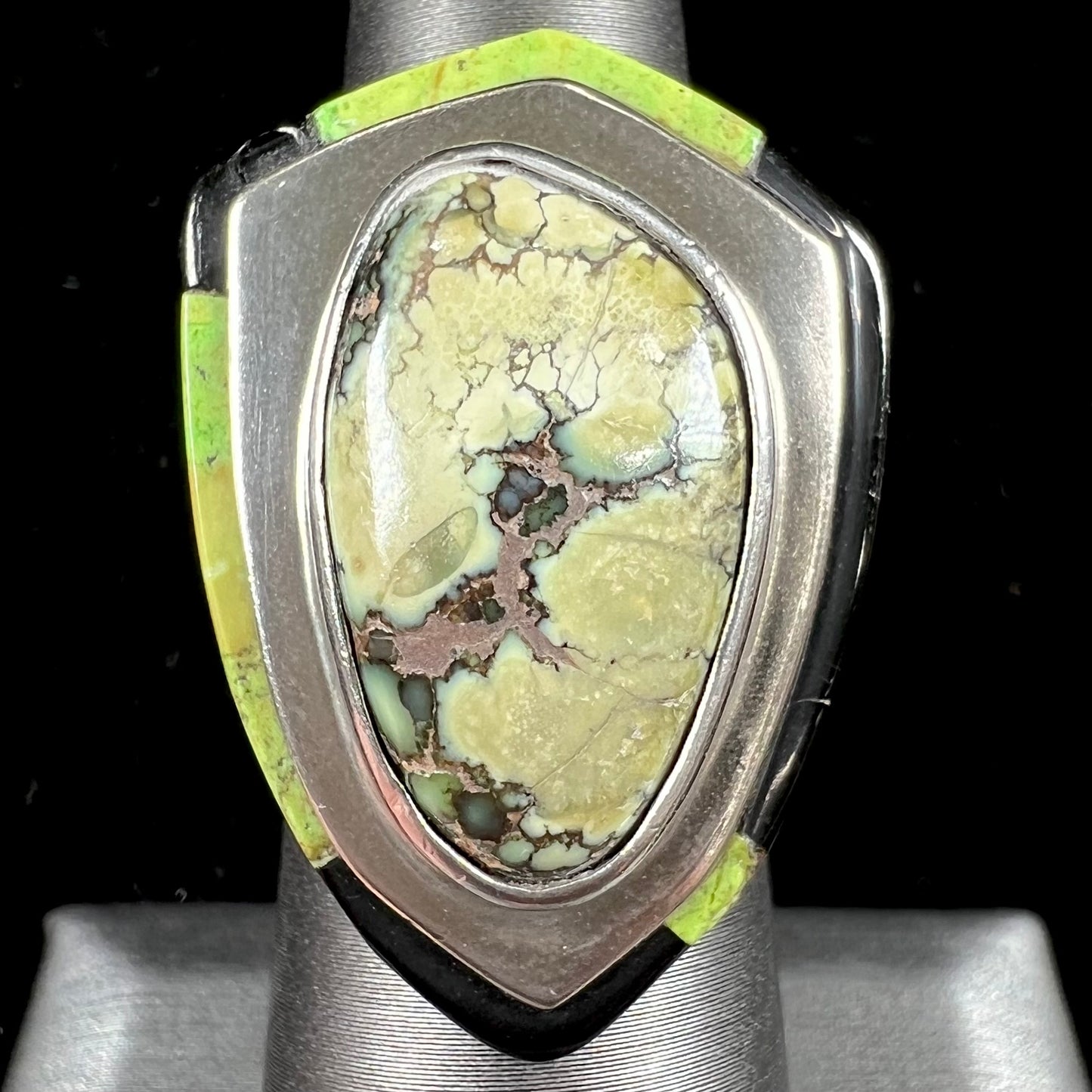 A shield shaped silver ring bezel set with a green gaspeite stone with stone inlaid edges, handmade by artist Benny Armijo.