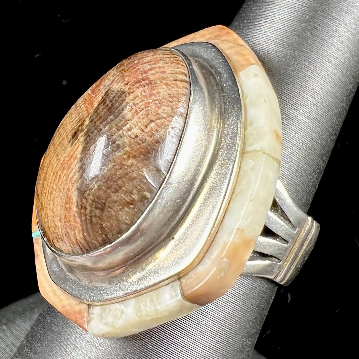 A silver ring handmade from a bezel set petrified wood stone, surrounded by quartz, carnelian, and bone inlay.