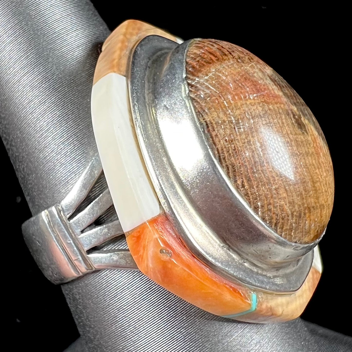 A silver ring handmade from a bezel set petrified wood stone, surrounded by quartz, carnelian, and bone inlay.