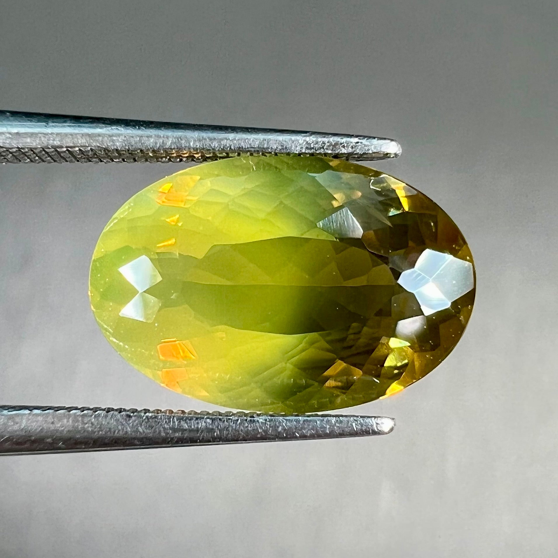 A loose, faceted oval cut bicolor chrysoberyl stone.  The stone goes from neon green to dark green with orangey red flashes.