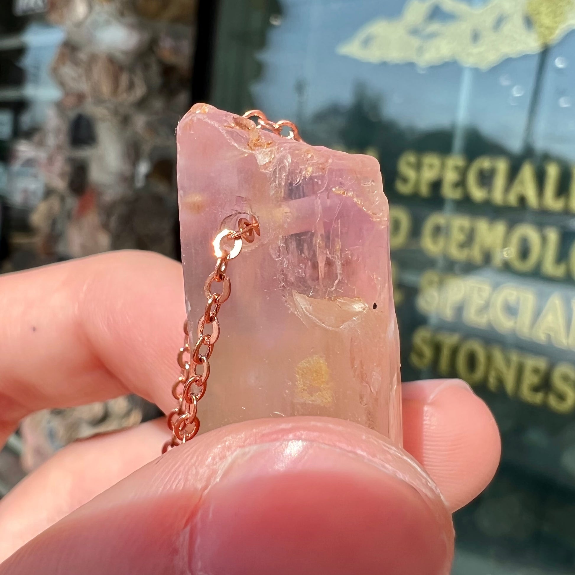 A drilled bicolor spodumene crystal hanging on a copper cable chain.  The crystal is pink and yellow, or kunzite and triphane respectively.
