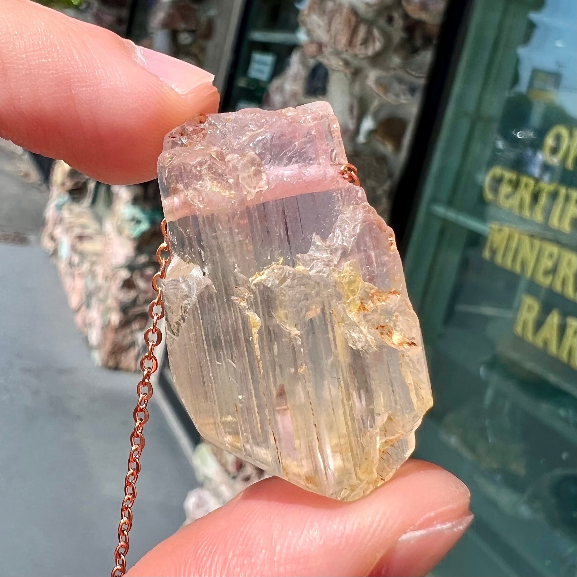 A drilled bicolor spodumene crystal hanging on a copper cable chain.  The crystal is pink and yellow, or kunzite and triphane respectively.