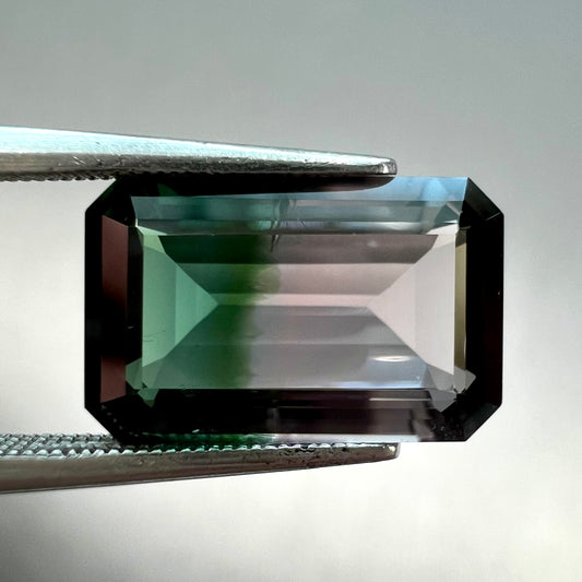 A loose, emerald cut bicolor tourmaline stone with a natural color separation of bluish green and light puce.