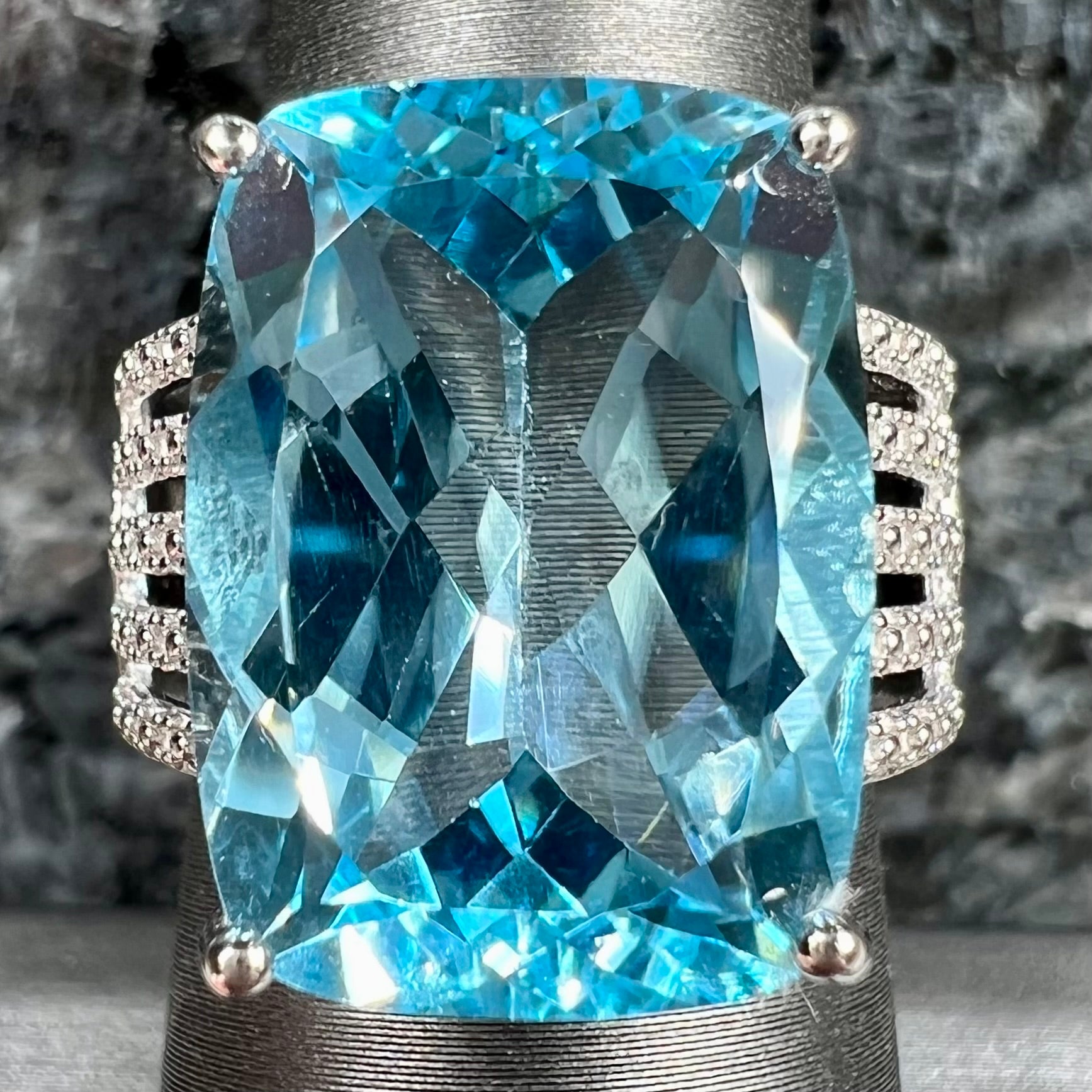 A sterling silver ring prong set with a large, cushion cut sky blue topaz stone.  The shank has been textured to mimic accent stones.