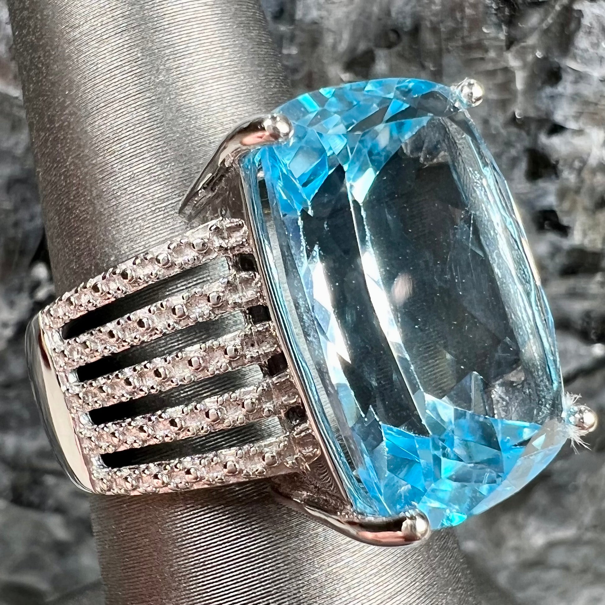 A sterling silver ring prong set with a large, cushion cut sky blue topaz stone.  The shank has been textured to mimic accent stones.