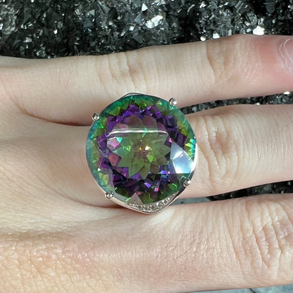 A large, round cut pink and green mystic topaz set in a sterling silver ring with white topaz accent stones.