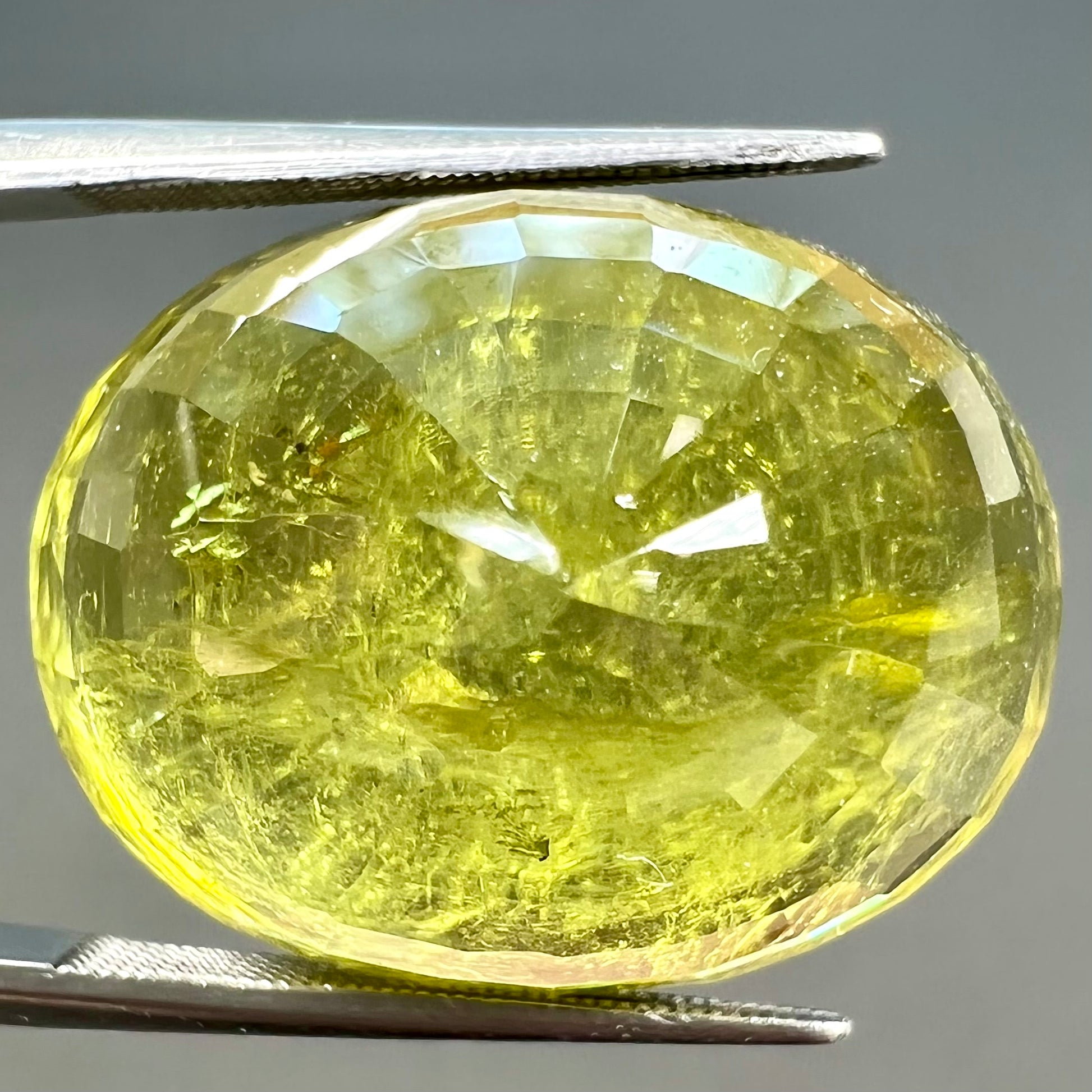 A loose, faceted oval cut green tourmaline stone.  The color is an almost neon yellow-green.