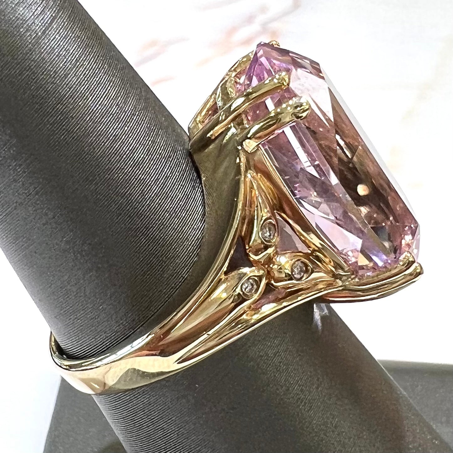 A large, pink kunzite is prong set into a 14kt yellow gold basket-style ring mounting with three diamonds flush set into the design on each side.