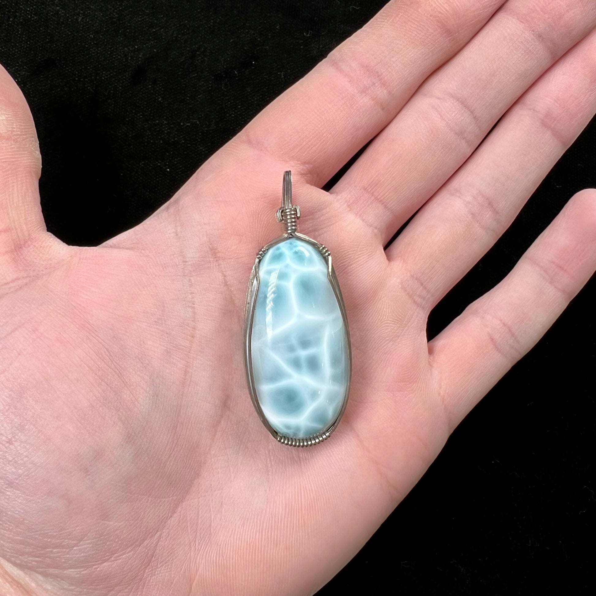 A large, oval cabochon cut blue larimar stone mounted in a sterling silver wire wrapped pendant.