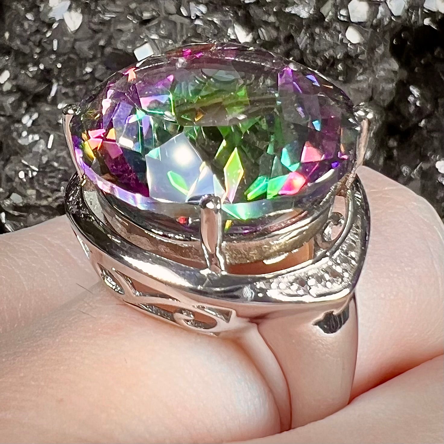 A large, round cut pink and green mystic topaz set in a sterling silver ring with white topaz accent stones.