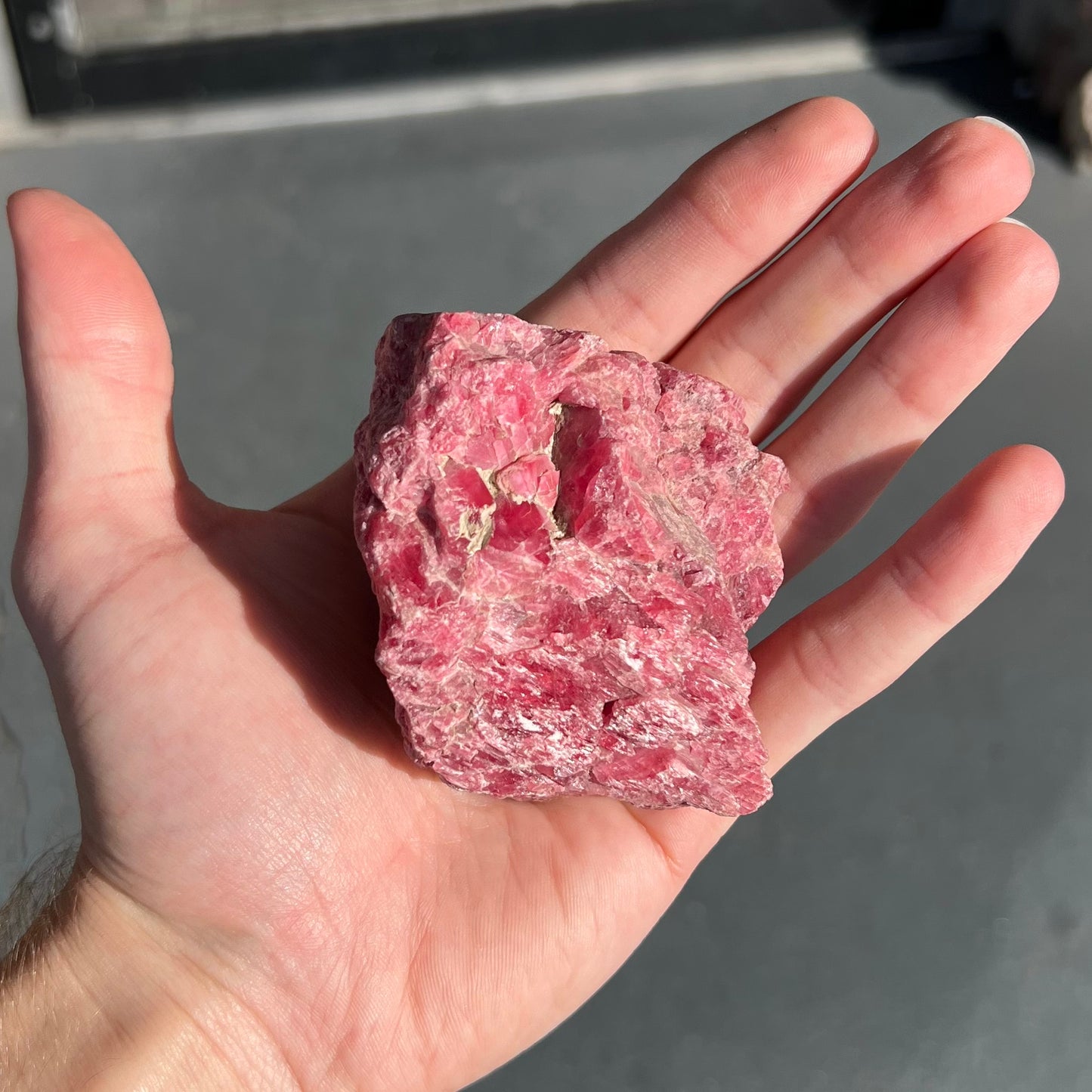 A rough pink rhodonite crystal specimen the size of a small fist.
