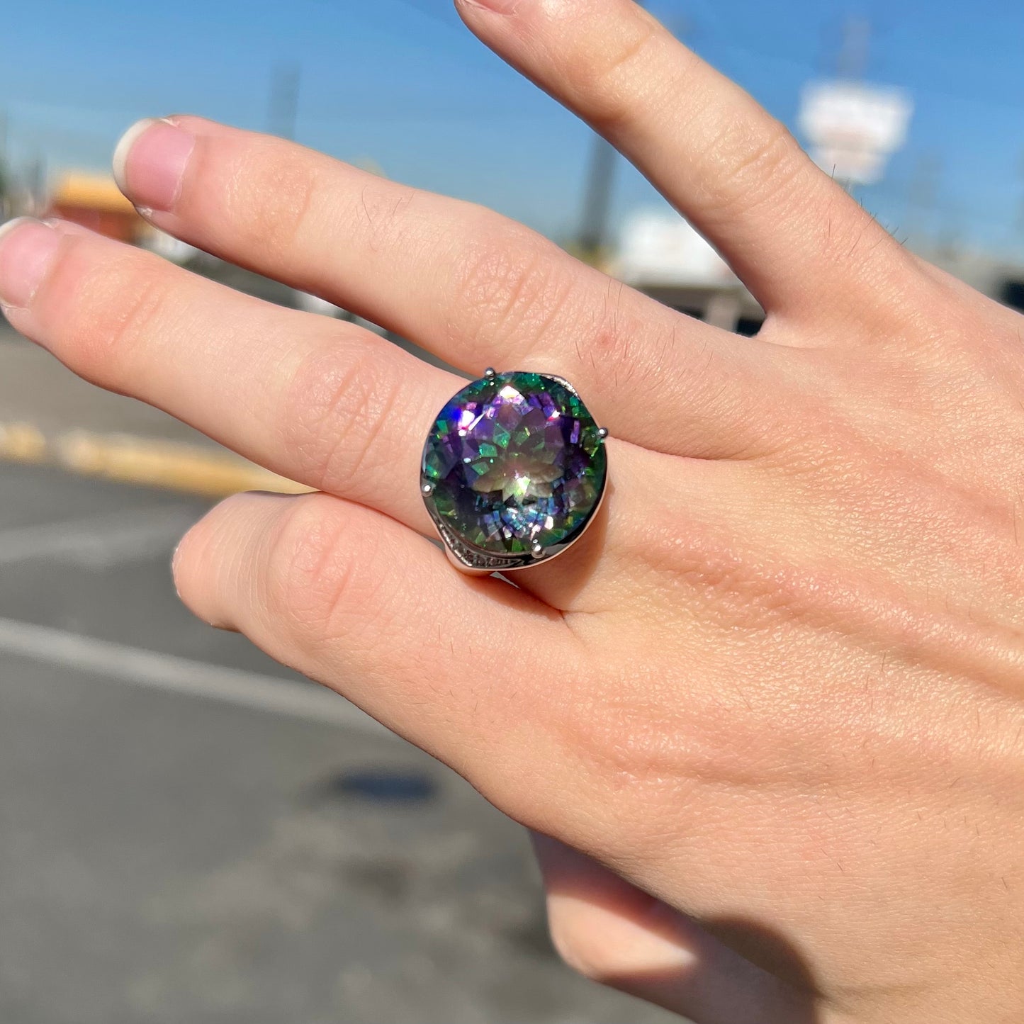 A large, round cut pink and green mystic topaz set in a sterling silver ring with white topaz accent stones.