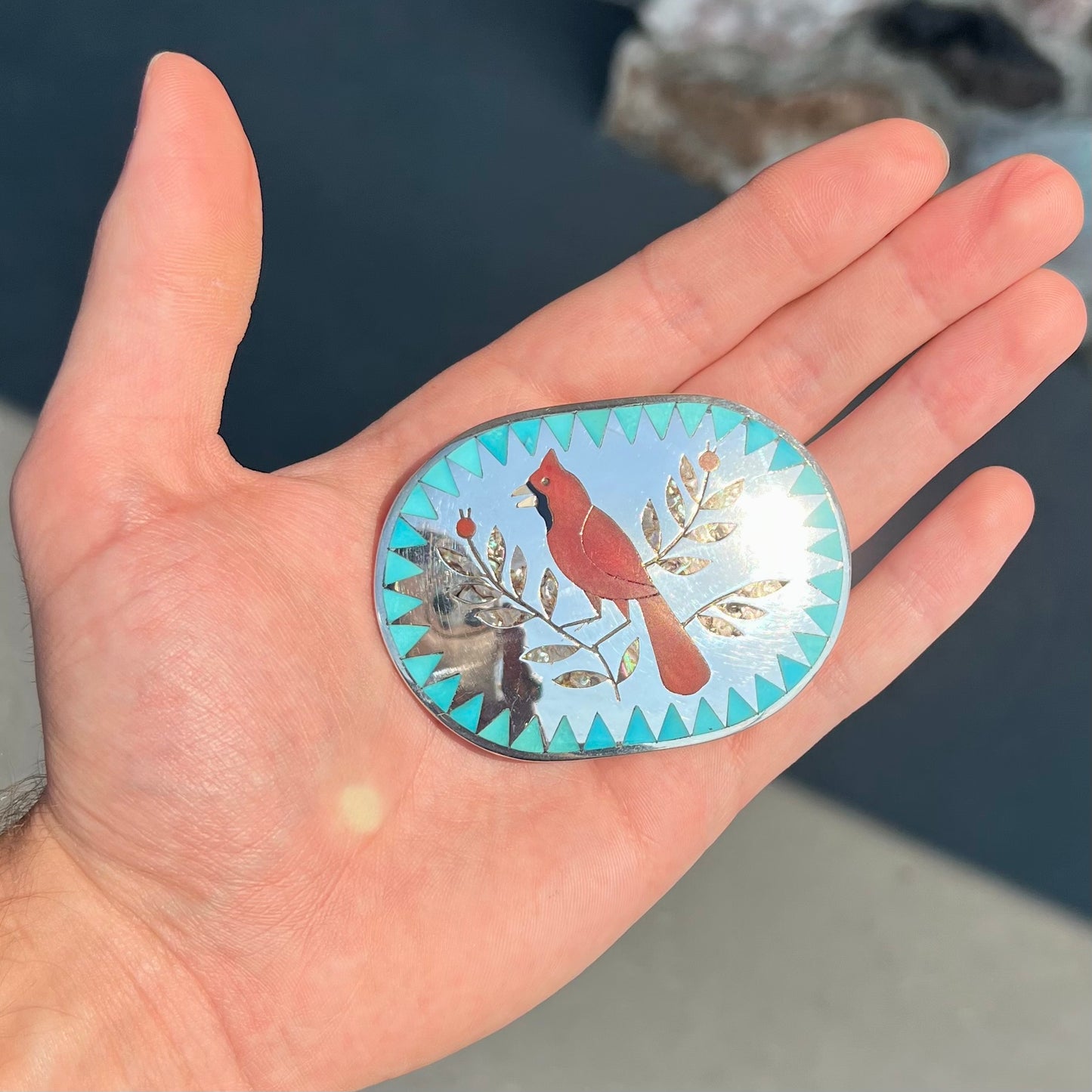 A Zuni belt buckle featuring a red cardinal inlaid with coral, handmade by artists Dennis and Nancy Edaakie.