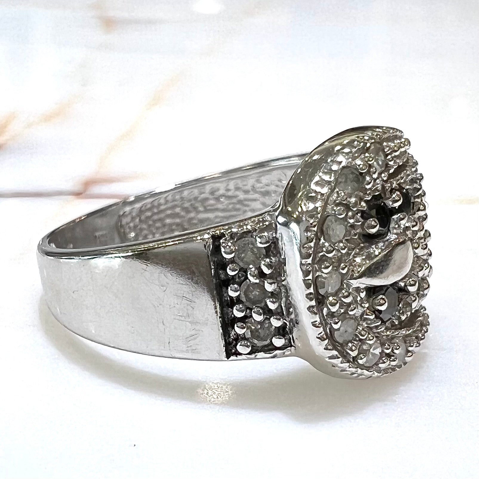 A white gold buckle ring pave set with round black and white diamonds.
