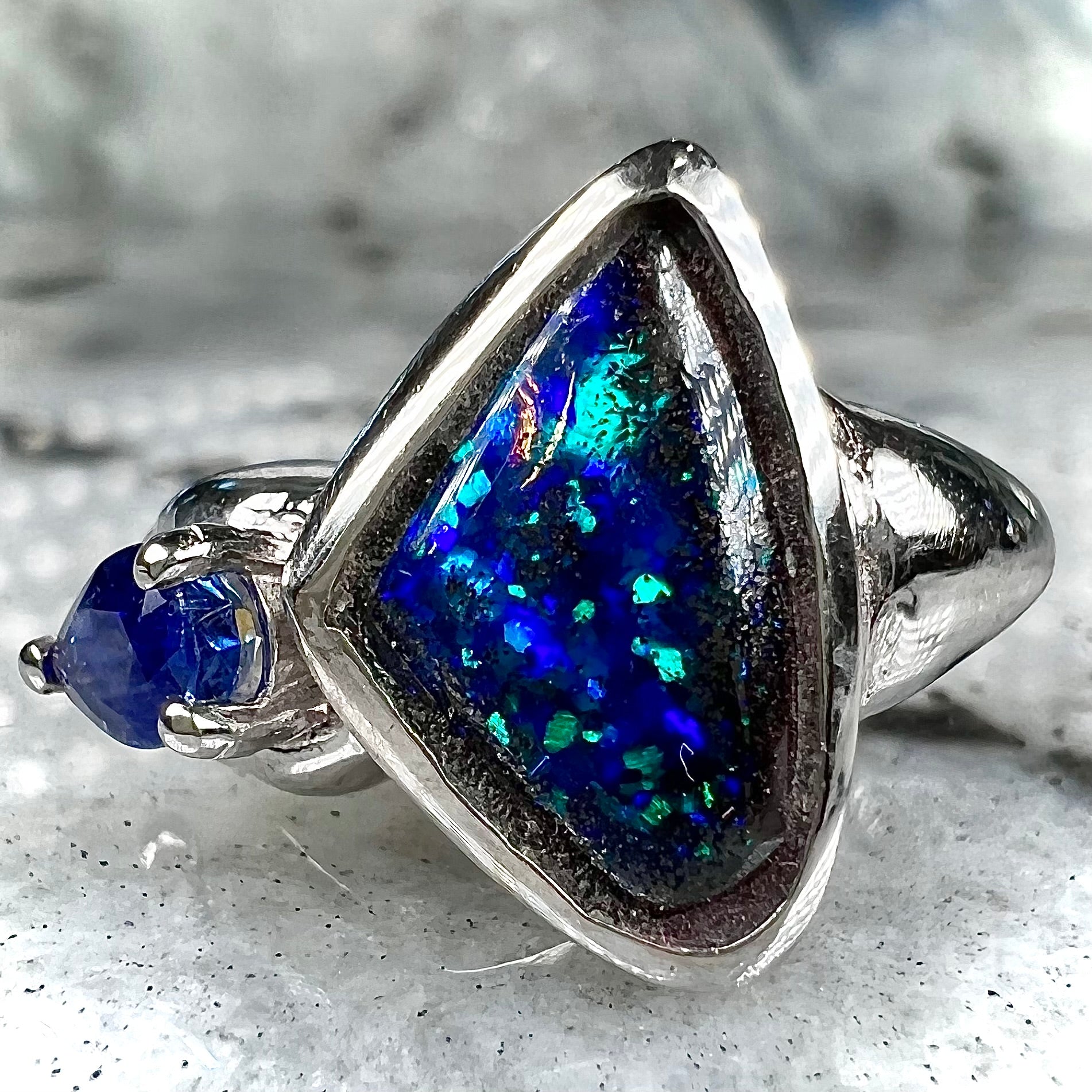 A ladies' white gold ring set with Australian black boulder opal and pear shape blue sapphire.
