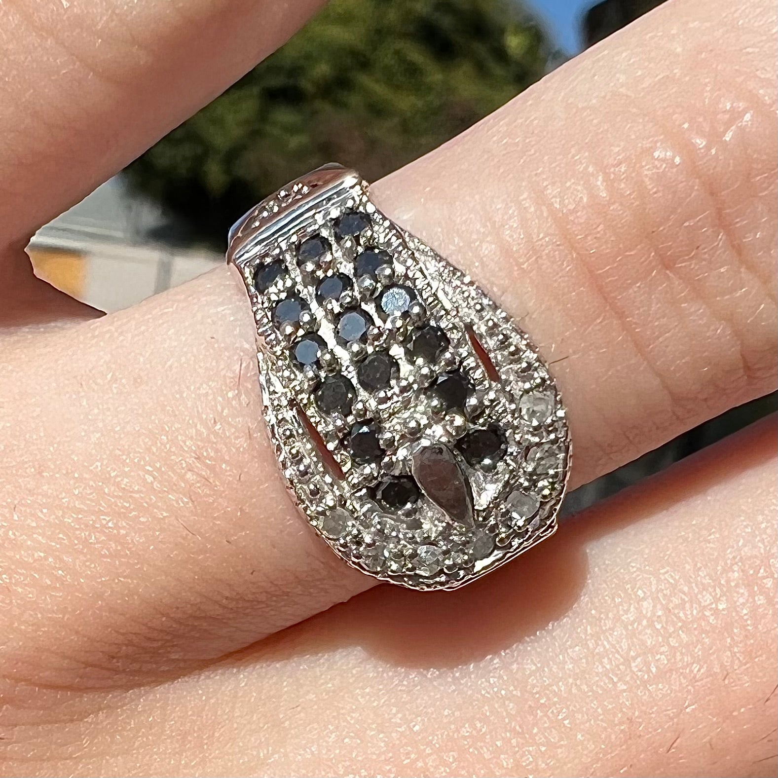 A white gold buckle ring pave set with round black and white diamonds.