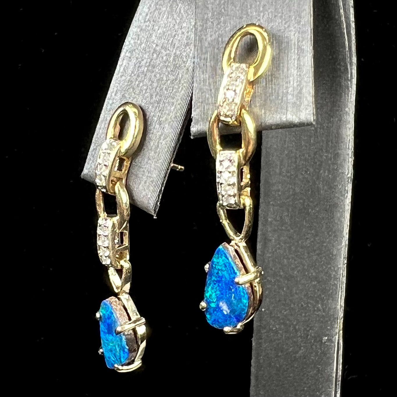 A pair of black opal doublet dangle earrings set in 10kt yellow gold with diamond accents.