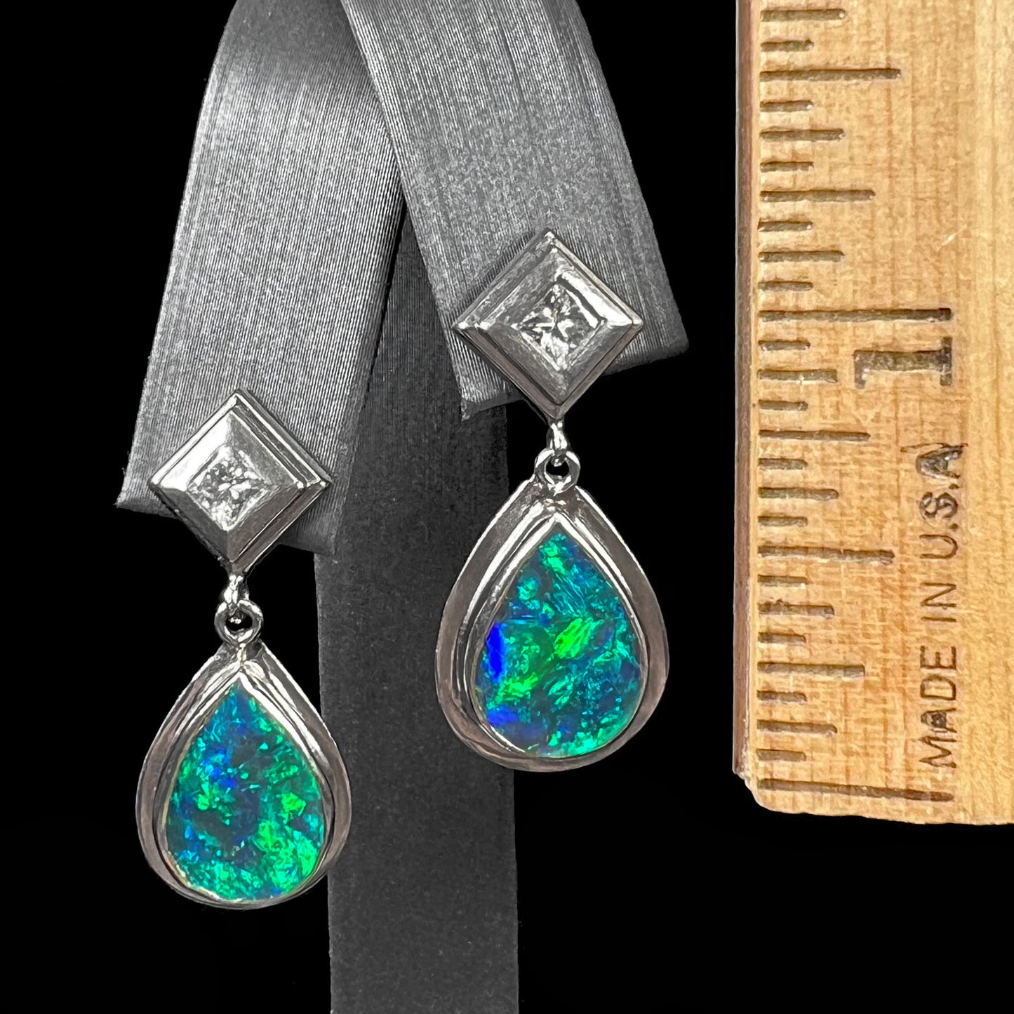 Black crystal opal dangle earrings with blue body color and green play of color set with princess cut diamonds in platinum.