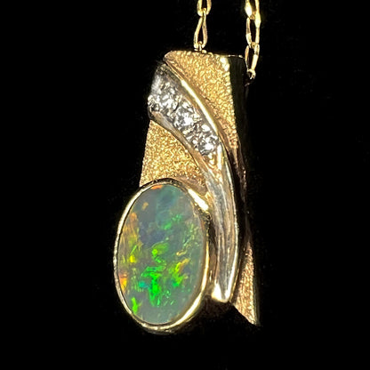 A yellow gold natural, Australian black opal necklace set with three round diamond accents.