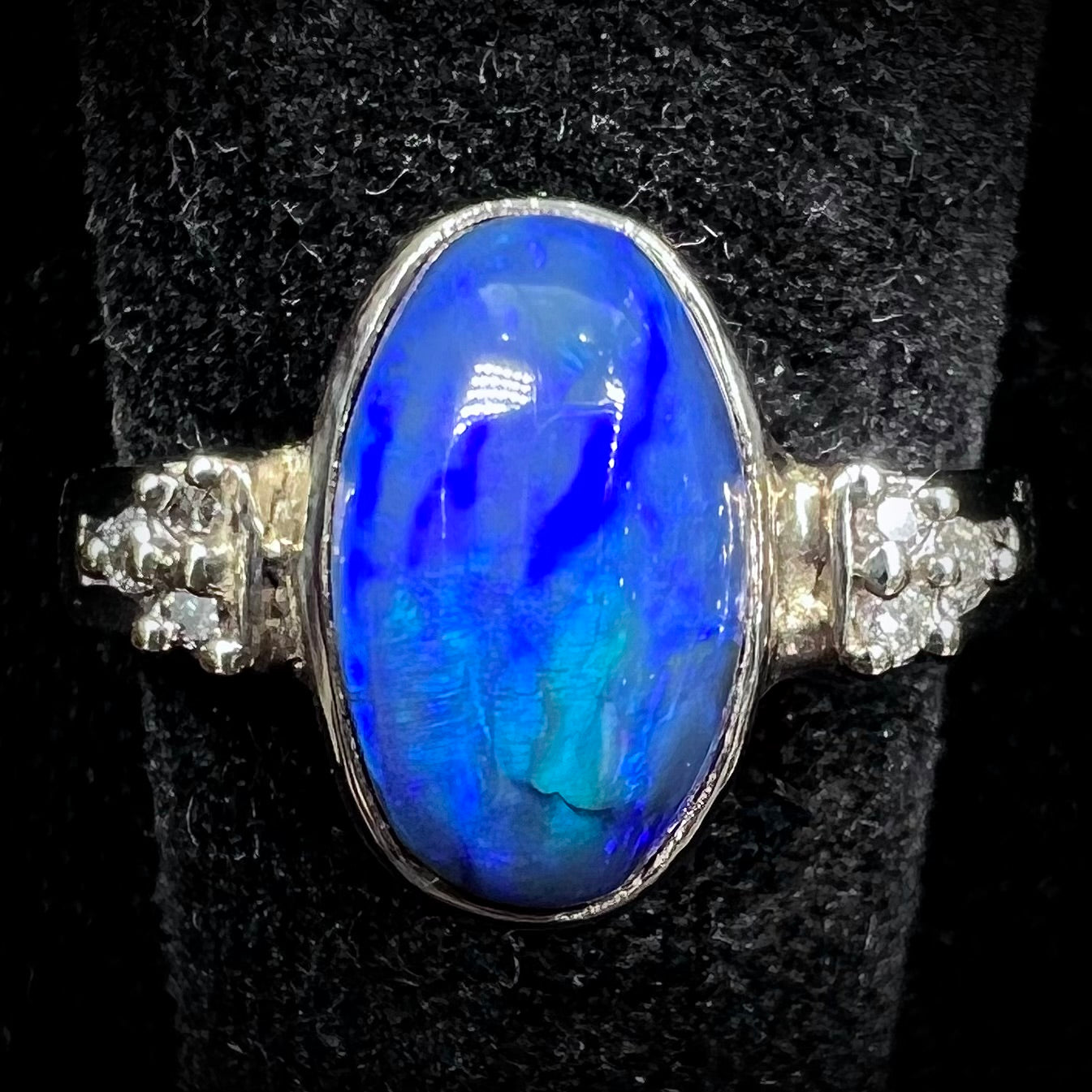 A white gold ring set with a Lightning Ridge black opal and diamond accents.  The opal displays a cat's eye pattern.