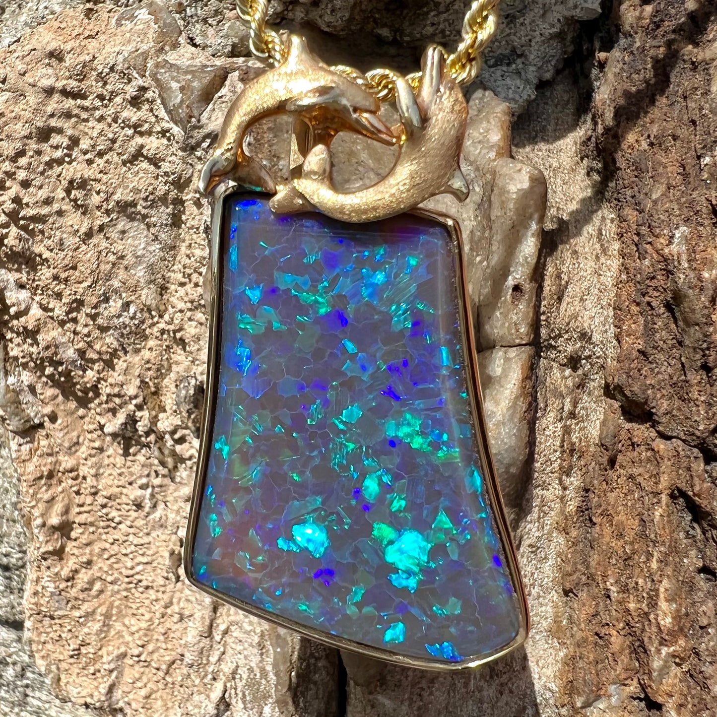 A gold freeform cut black opal bezel pendant cast with two dolphins on top of the opal.