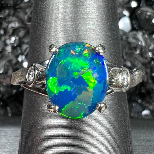 A white gold, oval cabochon cut black opal doublet ring set with two round diamond accent stones.