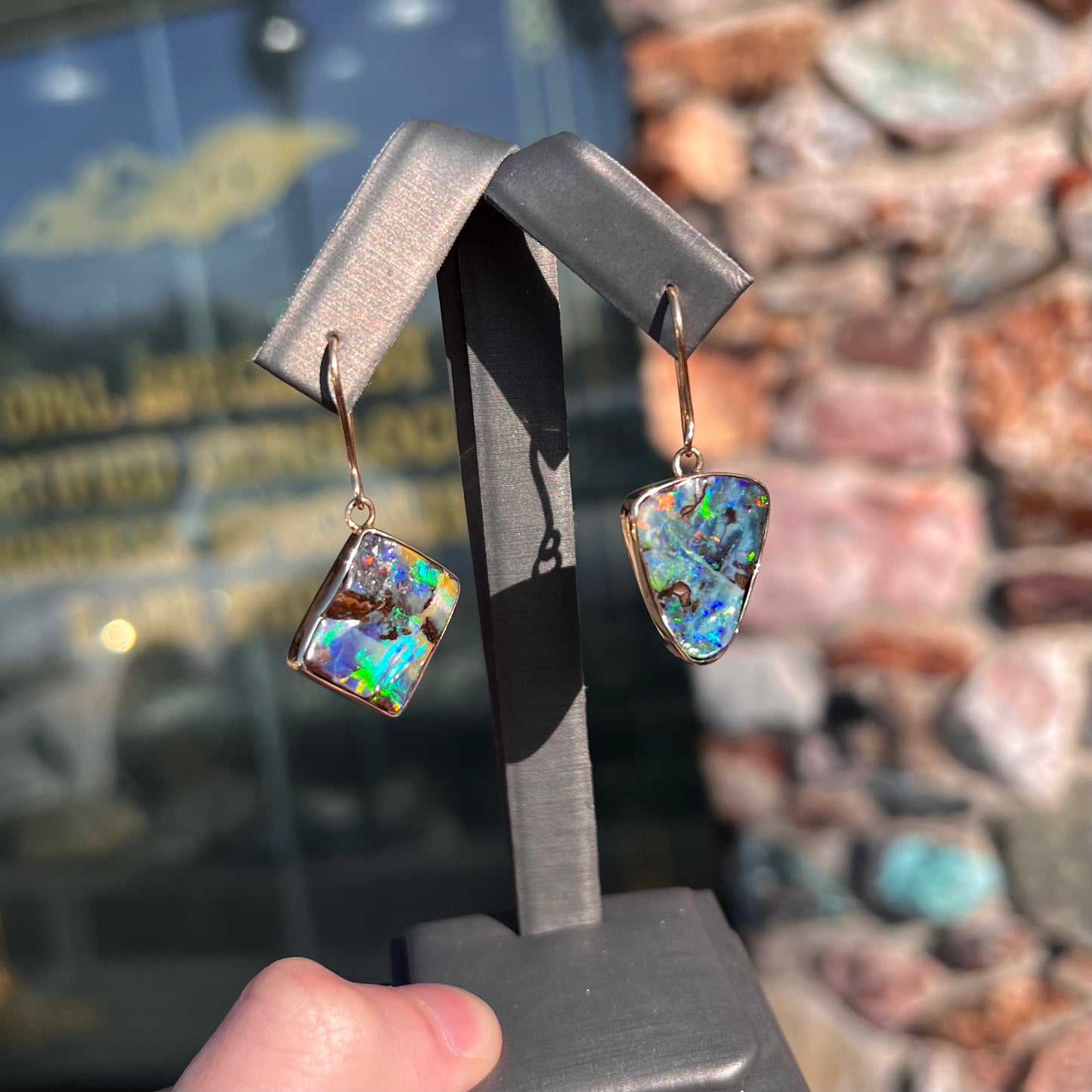 An asymmetric pair of French wire dangle yellow gold boulder opal earrings.  One opal is a square, and the other is a triangle.