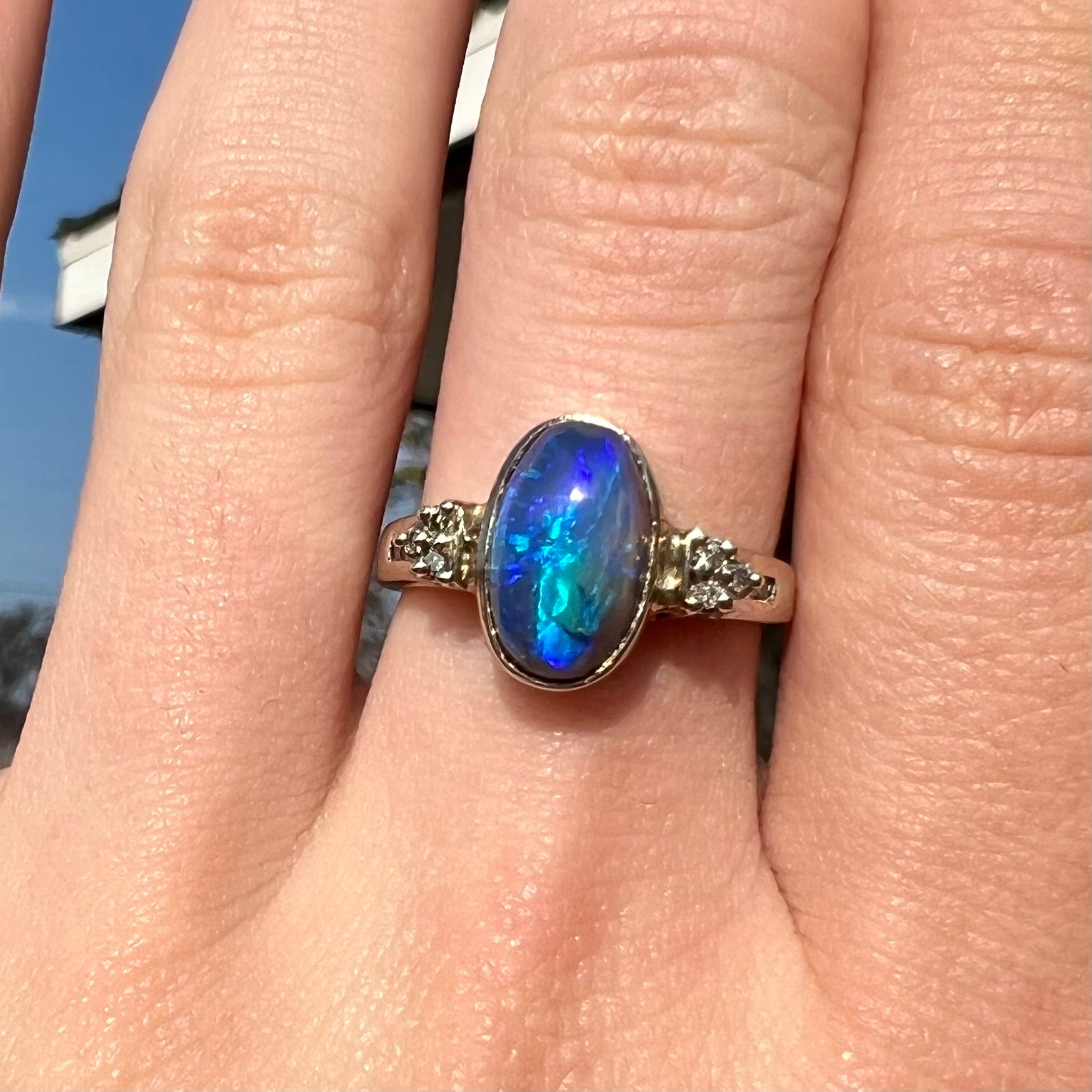 A white gold ring set with a Lightning Ridge black opal and diamond accents.  The opal displays a cat's eye pattern.