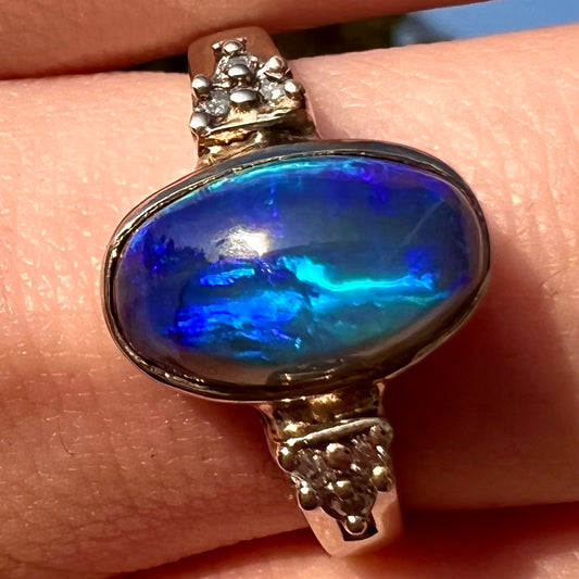 A white gold ring set with a Lightning Ridge black opal and diamond accents.  The opal displays a cat's eye pattern.