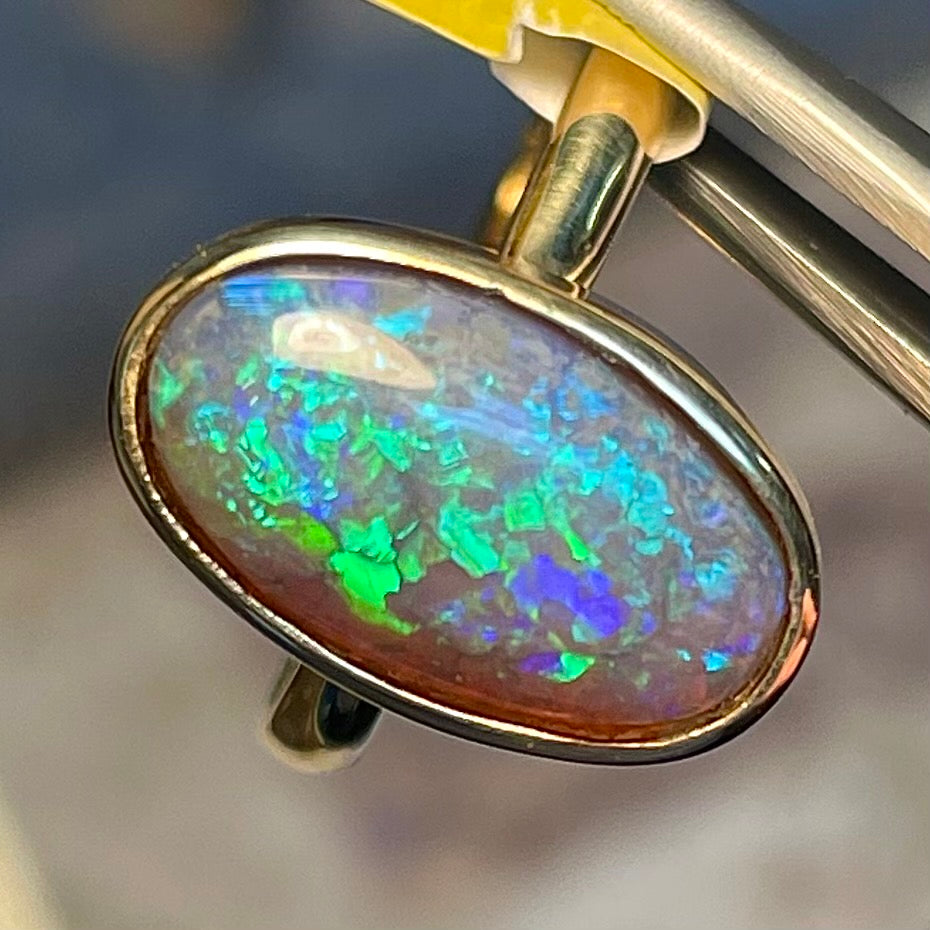 A simple yellow gold solitaire ring with a bezel set Lightning Ridge black crystal opal from Australia.