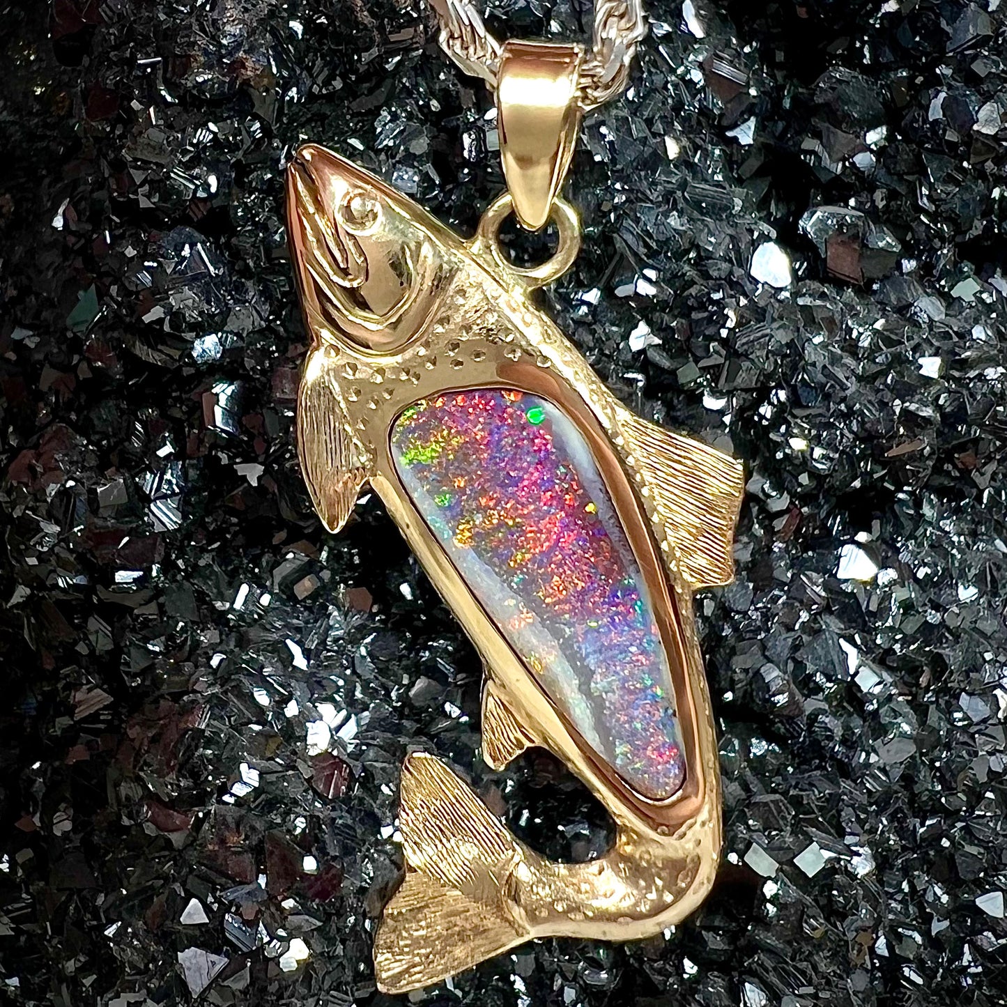 A yellow gold fish pendant detailed to look like a rainbow trout.  The body of the fish is set with a color changing black opal stone.